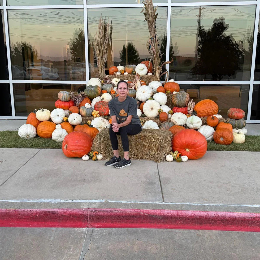 Woman sitting on hay bale surrounded by colorful pumpkin display for fall porch decor in Dallas-Fort Worth